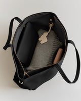 Open tote bag with a folded sweater, pouch, and a small keychain inside.