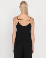 Woman standing with her back facing the camera wearing a tank top with crisscross straps.