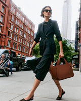 Person walking in city wearing a blazer and skirt and carrying a large bag