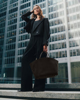 Person in suit standing on steps holding a large bag, skyscrapers in background.