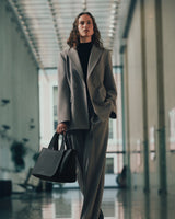 Person in suit holds a handbag walking in a corridor with large windows.