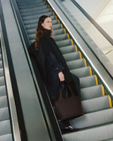 Person on escalator holding a large bag, wearing a coat.