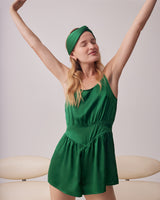 Woman stretching arms in a romper and headband, standing indoors.