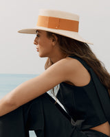 Woman in a hat looking over her shoulder near the sea.