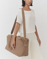 Person carrying a travel bag over shoulder wearing a short-sleeved top and pants.