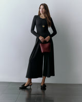 Woman wearing a long-sleeve top, wide-leg pants, and holding a small handbag.