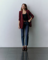 Person stands against a wall, wearing a red blazer, black top, jeans, and loafers.