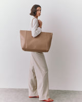 Person holding large tote bag, wearing long-sleeve top and wide-leg pants