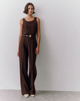 Person wearing a sleeveless top and trousers with a belt, standing against a plain background.