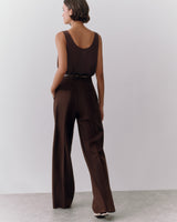 Person in a sleeveless top and wide-leg pants standing against a plain backdrop.