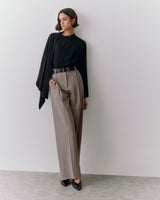Person wearing a sweater and trousers, standing against a wall.