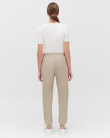 Woman standing with her back to the camera, wearing a top and pants.