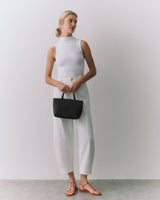 Person posing with a handbag, wearing sleeveless top and trousers.