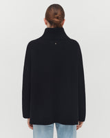 Woman wearing a turtleneck and jeans, viewed from behind with hair up.