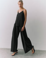 Woman in a a silk cami and wide-leg pants, wearing heels and a necklace.