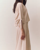 Person wearing loose top and wide-leg pants standing against plain backdrop