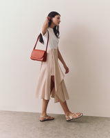 Person walking with shoulder bag and wearing sandals and a skirt.