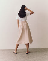 Person wearing a T-shirt and skirt, facing away, standing on a plain floor.