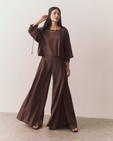 Woman wearing wide-legged pants and loose top, standing on a plain background.