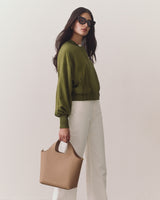 Woman in a jacket and pants holding a handbag wearing sunglasses
