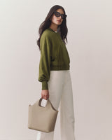 Person wearing sunglasses, holding a handbag, dressed in a jacket and pants.