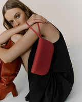 Person in dress sitting with shoulder bag and knee-high boots.