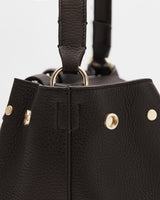 Close-up of a textured handbag with metal rings and studs.