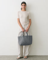 Person holding a large tote bag while wearing a short sleeve shirt and wide-leg pants