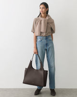 Person holding large tote bag, wearing sweater, jeans, and boots.