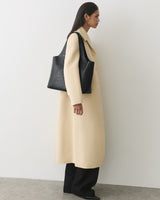 Person in long coat holding a croc-embossed leather bag over shoulder.