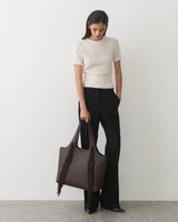 Person holding a fringed tote bag, wearing a short-sleeve top and long pants.