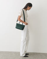Person standing, holding a shoulder bag, wearing a short-sleeve top and pants.