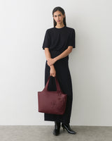 Person holding a floral tote bag standing in front of plain wall.