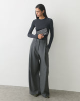 Person in long-sleeve top and wide-leg pants holding a croc-embossed leather clutch.