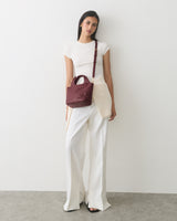 Person standing with a shoulder bag with a floral detail, wearing a top and wide-leg pants.