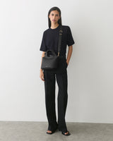 Person wearing a T-shirt and pants, holding a handbag with a shoulder strap.