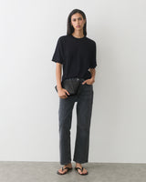 Person standing wearing a T-shirt, jeans, and sandals, holding a clutch.
