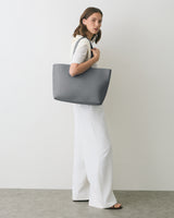 Person holding large handbag, standing against plain background wearing long pants.