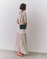 Person in long skirt and sweater with a small shoulder bag and sandals standing sideways