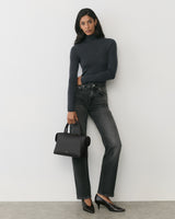 Person in turtleneck and jeans holding handbag, wearing heels.