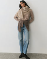 Person wearing a scarf, sweater, and jeans, standing against a plain background