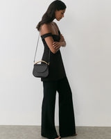 Woman in sleeveless top and pants with a handbag over shoulder standing sideways.