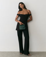 Person in strapless outfit holding a small purse, standing against a plain backdrop.