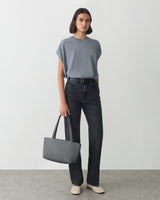 Person stands holding a handbag, wearing a t-shirt and jeans.