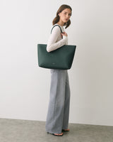 Person holding large tote bag, wearing long-sleeve top and wide-leg pants.