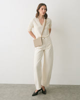 Person wearing a top, pants, and crossbody purse, standing on a plain background.