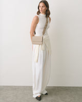 Person wearing a sleeveless top, long skirt, and crossbody bag standing indoors.