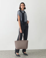 Person posing with large handbag in one hand and wearing casual outfit with cape draped over shoulders.