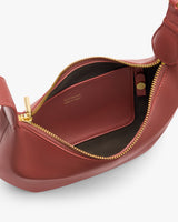 Open handbag with zipper and inner pocket showing branding and small tube inside.