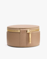 Round leather jewelry case with zipper and small tag on front.